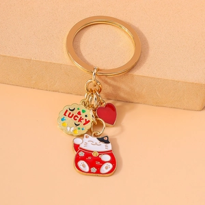 Golden Lucky Cat keychain with red heart and engraved metal disc on a soft beige surface