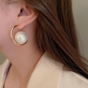 Close-up of stylish C-shaped golden earrings with a large white pearl on female model