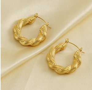 Gros plan de boucles d'oreilles créoles torsadées dorées sur satin champagne
