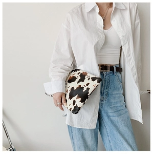 Detail view of a cow print envelope clutch bag held by a model in a casual outfit
