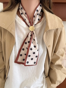Close-up of silk neck scarf with black polka dots and a gold circular metal buckle