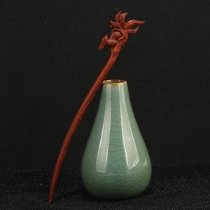 Macro detail of hand-carved phoenix pattern on a dark sandalwood hair pin in a vase