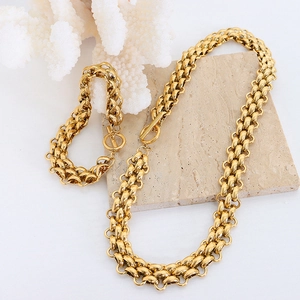 Chunky gold chain link necklace and bracelet set displayed on a beige stone slab