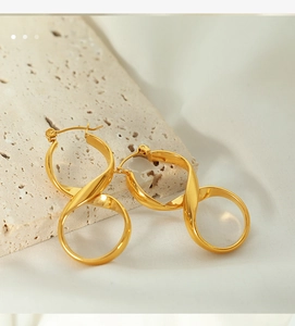 Macro shot of gold twisted knot hoop earrings on textured stone and silk fabric