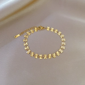 Detailed macro view of a gold four-leaf clover chain bracelet made of polished titanium steel