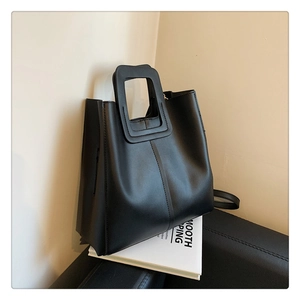 Detail of black leather bucket bag featuring unique rectangular cutout handle on books