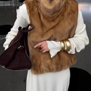 Gilet in ecopelliccia marrone da donna con abito bianco e gioielli dorati