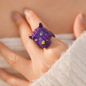 Gros plan détaillé d'une bague tête de panthère violette avec points roses sur un doigt.
