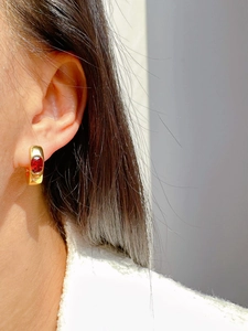 Close-up of elegant gold U-shaped earrings with oval red ruby gemstone worn on ear