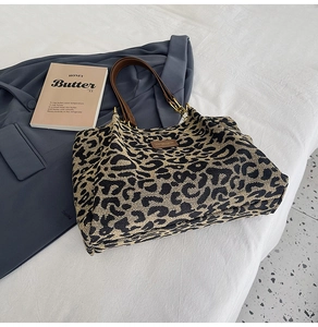Detail of leopard print tote bag with brown PU strap and metal hardware on white bed
