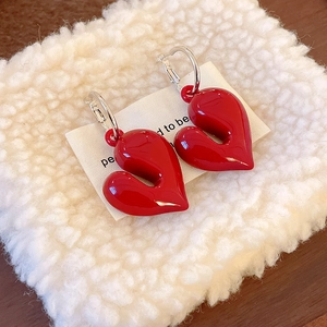 Detail of red heart-shaped hoop earrings on soft plush background with luxury packaging