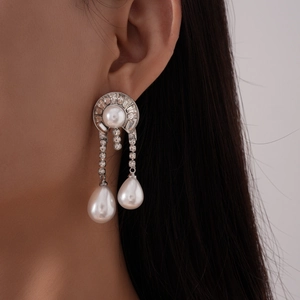 Close-up of elegant silver drop earrings with white pearls and sparkling diamonds on model