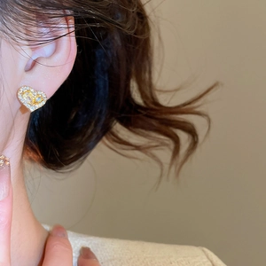 Close-up of heart-shaped gold-plated stud earring with clear zircon on earlobe