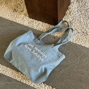 Detail of light blue denim tote bag with white Less Mondays More Sundays embroidery
