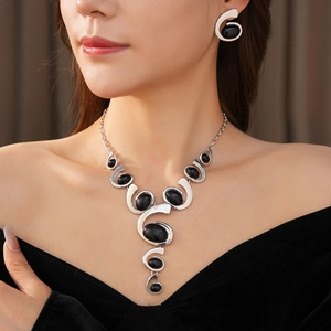 Close-up of silver geometric necklace and earrings set with black oval stones on a model