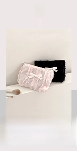 Dettaglio di pochette trucco in pizzo con fiocchi e pois su supporto bianco minimal