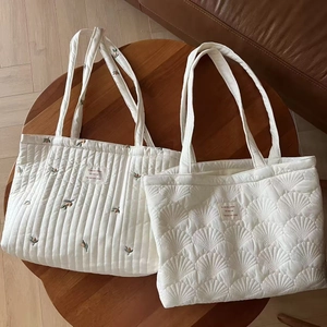 Detailed view of cream quilted tote bags with floral embroidery on a wooden table