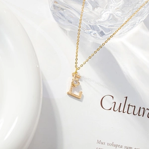 Detailed view of golden letter E necklace with a zircon flower on an elegant magazine background