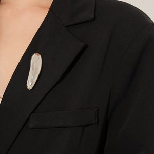Close-up of a fluid silver metal brooch on a black suit lapel with high-gloss finish