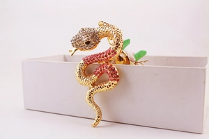 Close-up of golden snake keychain with red and clear rhinestones on a white gift box