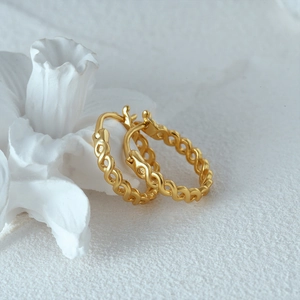 Detail view of gold infinity cross hoop earrings on a textured white surface with floral decor