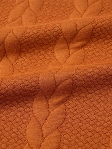 Detailed macro view of orange knitted sweater fabric with leaf-like jacquard texture