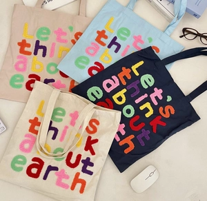 Close-up of four canvas tote bags with colorful towel-stitched eco slogan embroidery