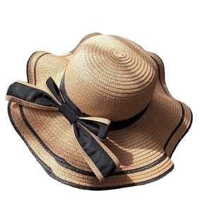 Elegant wide brim straw hat with black ribbon bow and wavy trim for beach sun protection