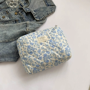Detailed view of blue floral quilted cosmetic bag with woven label and fabric texture