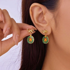 Detail of Christmas wreath earrings with gold bows and bells worn by a model