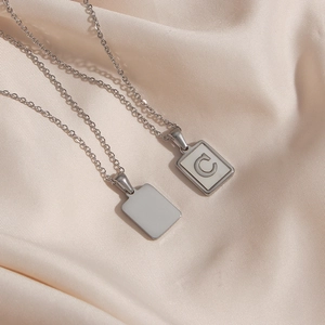 Detailed close-up of a silver necklace featuring a square pendant with white shell and letter C