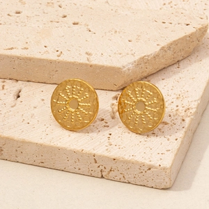 Detailed view of gold round stud earrings with radial dotted relief on stone background