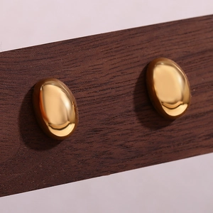 Dettaglio macro di orecchini a lobo ovali placcati oro 18K su trama in legno scuro