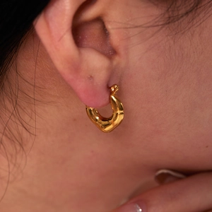 Close-up of irregular gold stainless steel heart earring worn on a model's earlobe
