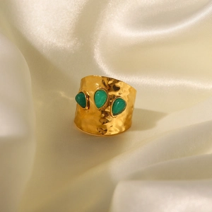 Detail view of gold stainless steel ring with three green gemstones on beige silk fabric