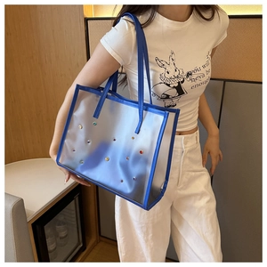 Blue transparent PVC tote bag with colorful rivets worn by a model in a modern room