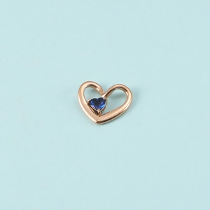 Détail d'un pendentif cœur en or rose avec une pierre bleue et un design ajouré élégant