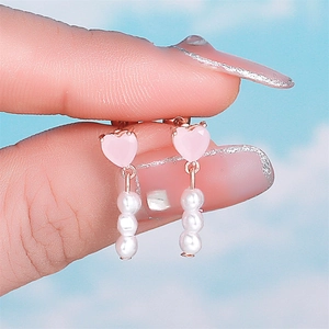 Detail of pink heart gem earring with triple pearl drop tassel held by hand