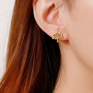 Close-up of golden tree of life stud earring worn on ear showing intricate metal detail