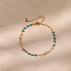 Close-up of golden chain bracelet with synthetic turquoise beads on linen texture