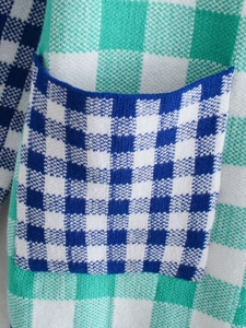 Detailed close-up of knit texture and pocket on a green blue white plaid cardigan