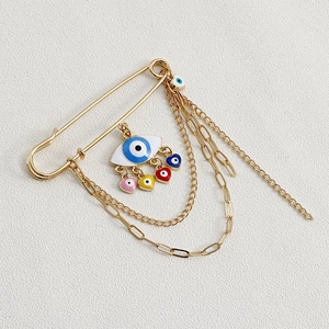 Detailed view of a gold safety pin brooch with colorful devil's eye charms and chains