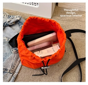 Macro detail of spacious orange drawstring bucket bag with makeup and power bank inside