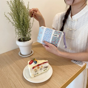 Close-up of small floral patchwork cotton pouch held by a woman in a cafe setting