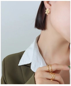 Macro detail of gold textured flower earrings and minimalist open ring on a model