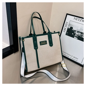 Detail of canvas tote bag showing green leather handles and brand logo patch