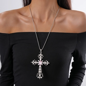 Close-up of a vintage silver cross necklace featuring a large pink gemstone and crystals