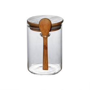 Clear glass storage jar with wooden lid and spoon attachment on a white background