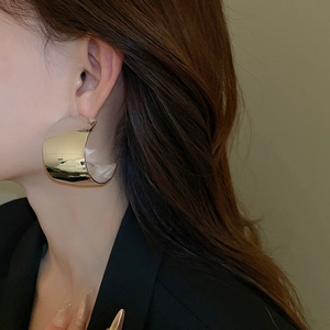 Close-up of chunky gold-plated C-hoop earring with a polished mirror finish on model