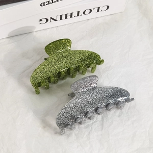 Simple glitter acrylic hair claws in green and silver shown on a stylish book background